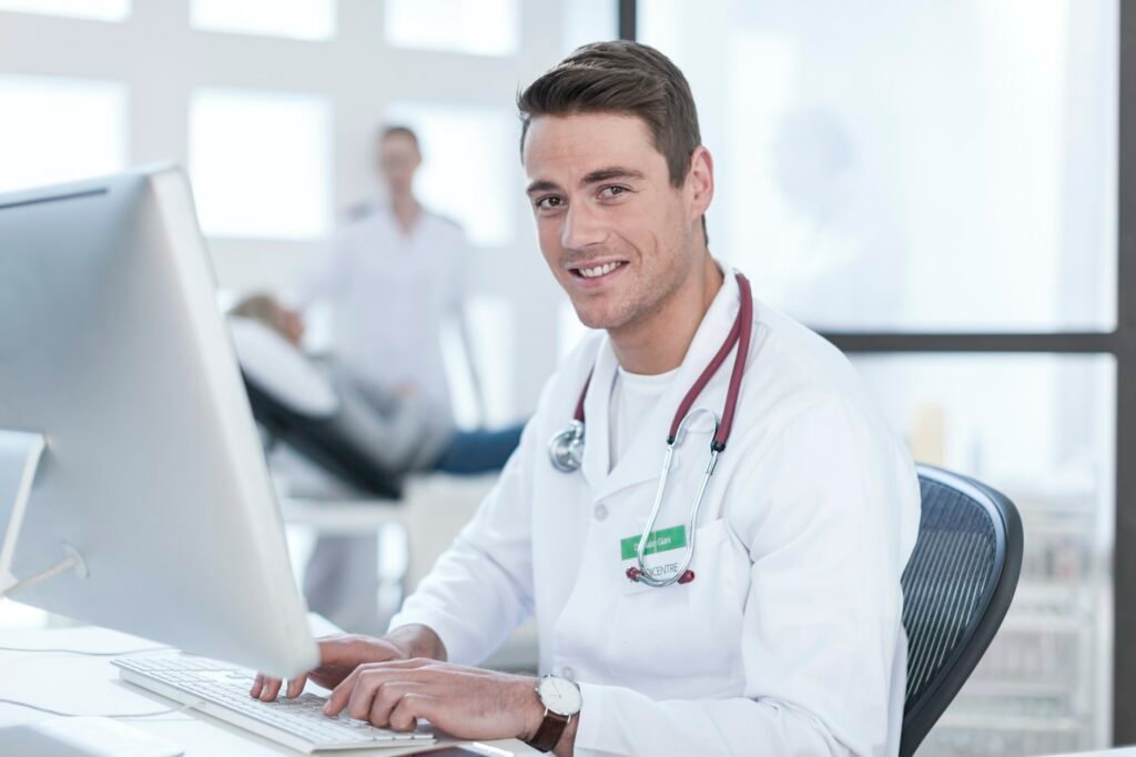 Portrait of smiling doctor sitting at desk working on computer